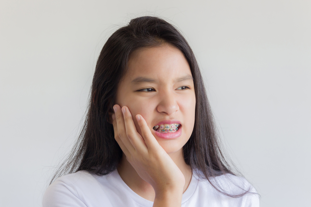 Image of girl wearing braces holding jaw as in they hurt her mouth.