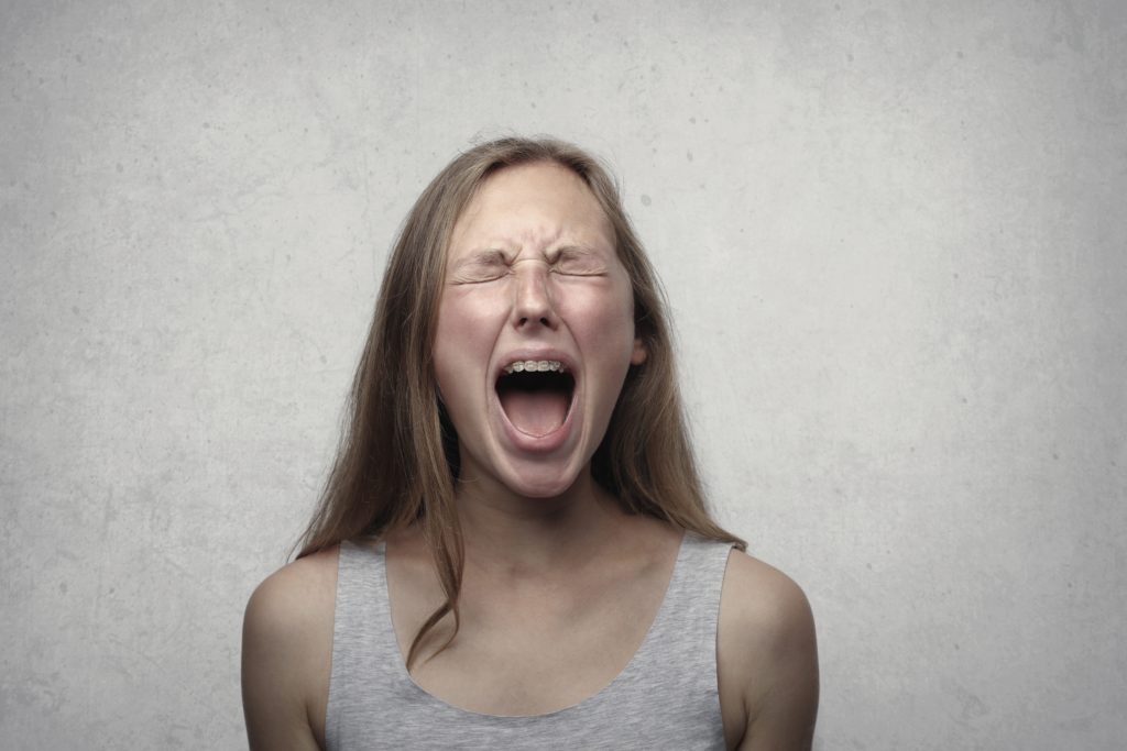Woman wearing gray tank top, yelling in frustration/pain