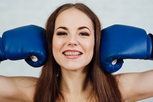 Image of woman wearing braces holding boxing gloves next to her head.