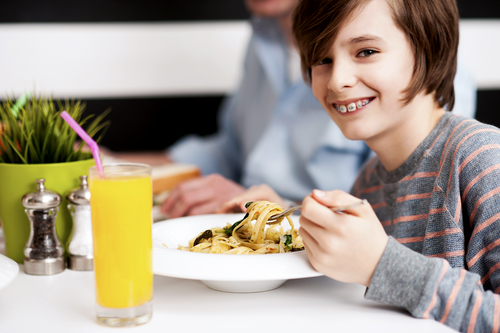 Image of boy wearing braces eating a bowl of pasta.