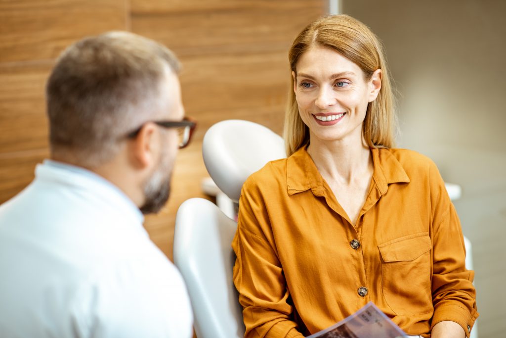 Woman sits in orthodontic chair, speaking with her orthodontist