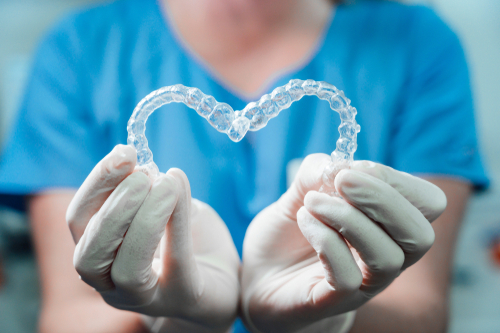 Image of an orthodontic assistant holding upper and lower invisalign pieces to form a heart shape.