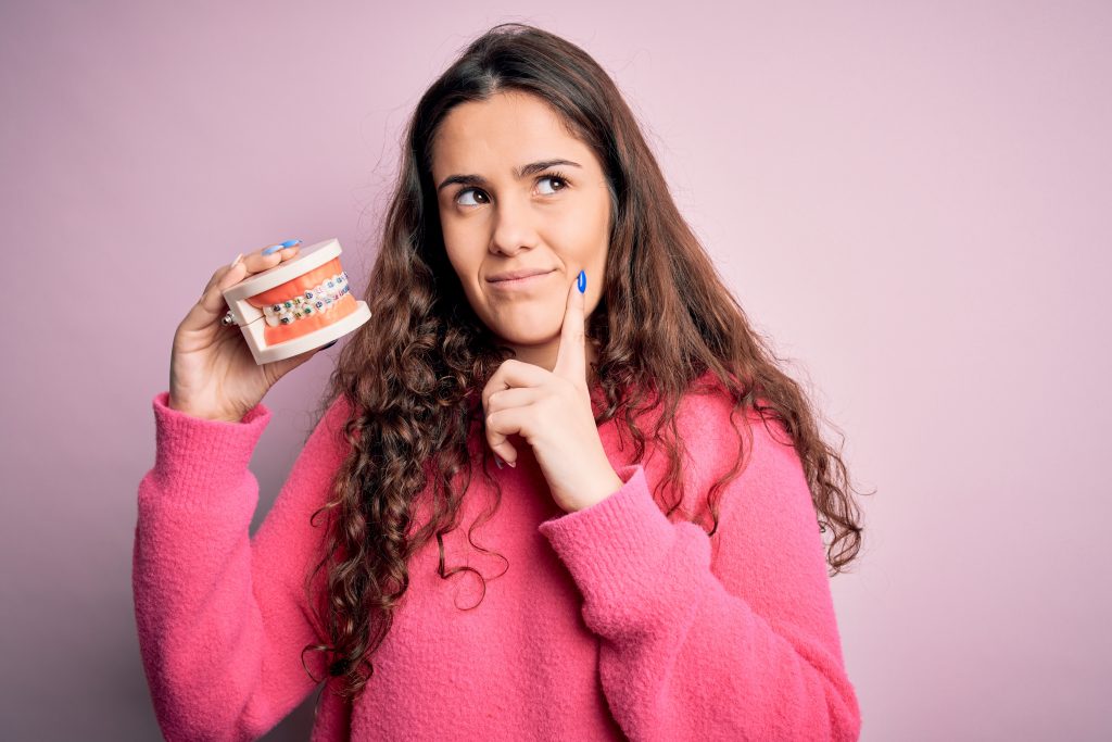 How Do Braces Work? 1 Woman inn a pink sweatshirt holding a dental mold, looking curious