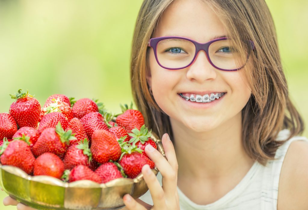 Young girl with glasses and braces hold s bowl of strawberries