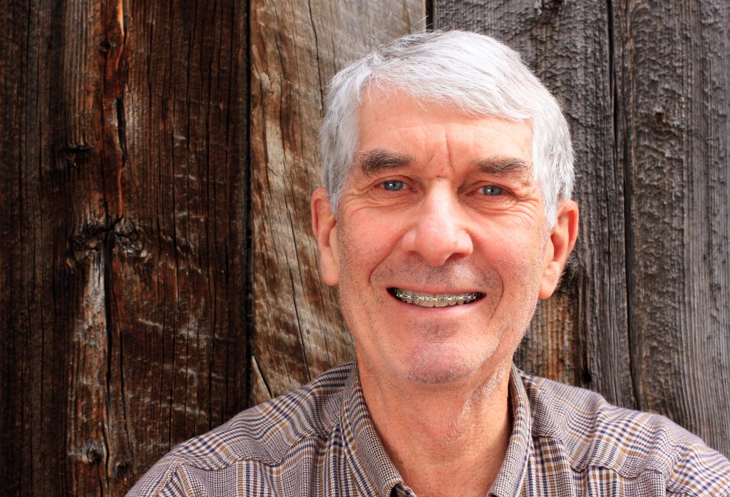 Elderly man with braces sit in front of a wood back drop