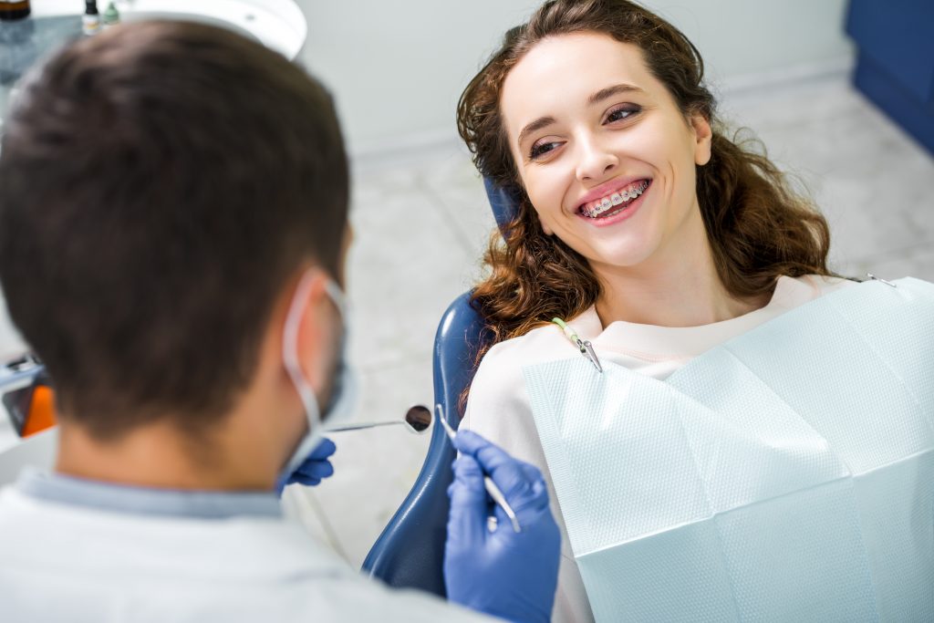 Young woman smiling with braces up at orthodontist