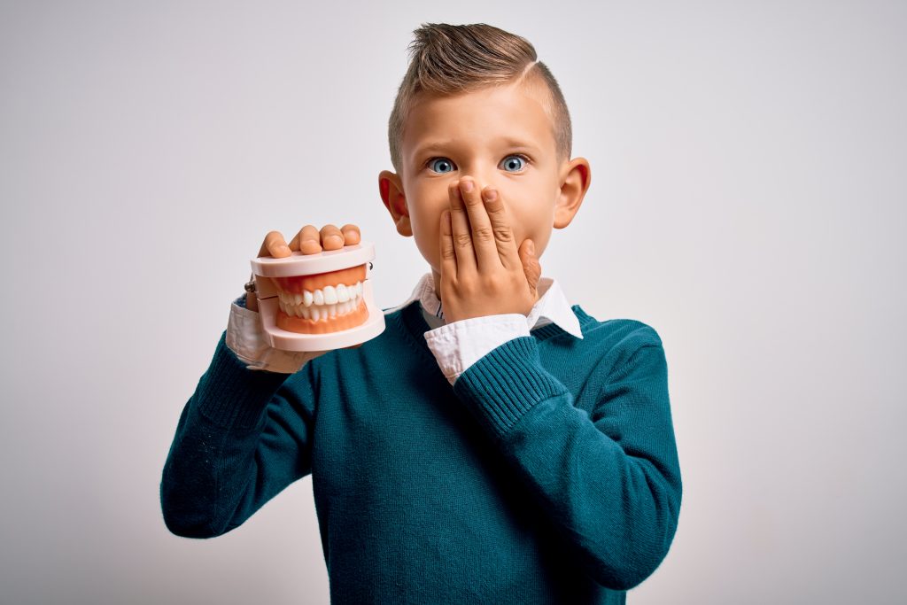 Young boy covering mouth in fear while holding an orthodontists dental mold