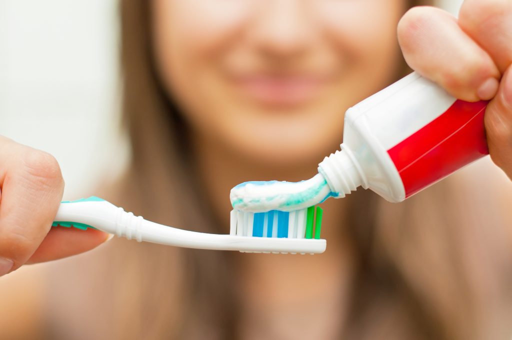 out of focus woman applies toothpaste to a tooth brush